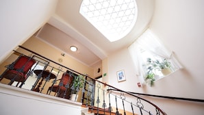 A staircase with a wrought iron railing, a round skylight, and a view of a room with a red chair and a potted plant. - Hotel Austria (Vienna)