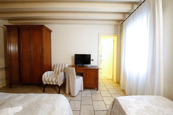 A hotel room with a bed, a desk with a television, a chair, and a wardrobe.