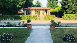 A pathway leading to a building with a red roof, surrounded by greenery and potted plants. - Relais Villa Selvatico (Roncade)