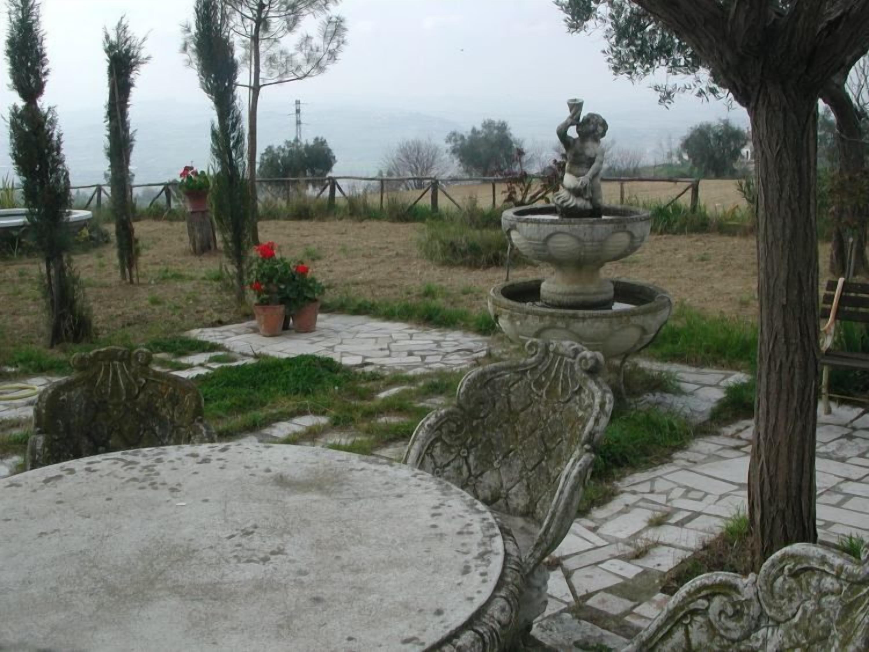 A garden with a stone table and chairs, a decorative fountain, and potted plants.