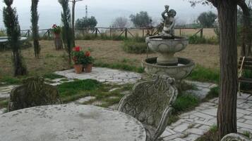 A garden with a stone table and chairs, a decorative fountain, and potted plants.