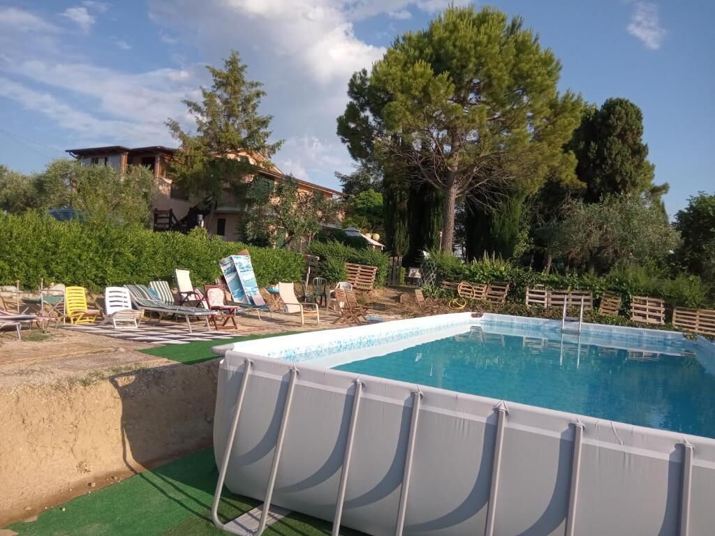 A swimming pool with lounge chairs and a wooden deck, surrounded by trees and a building.