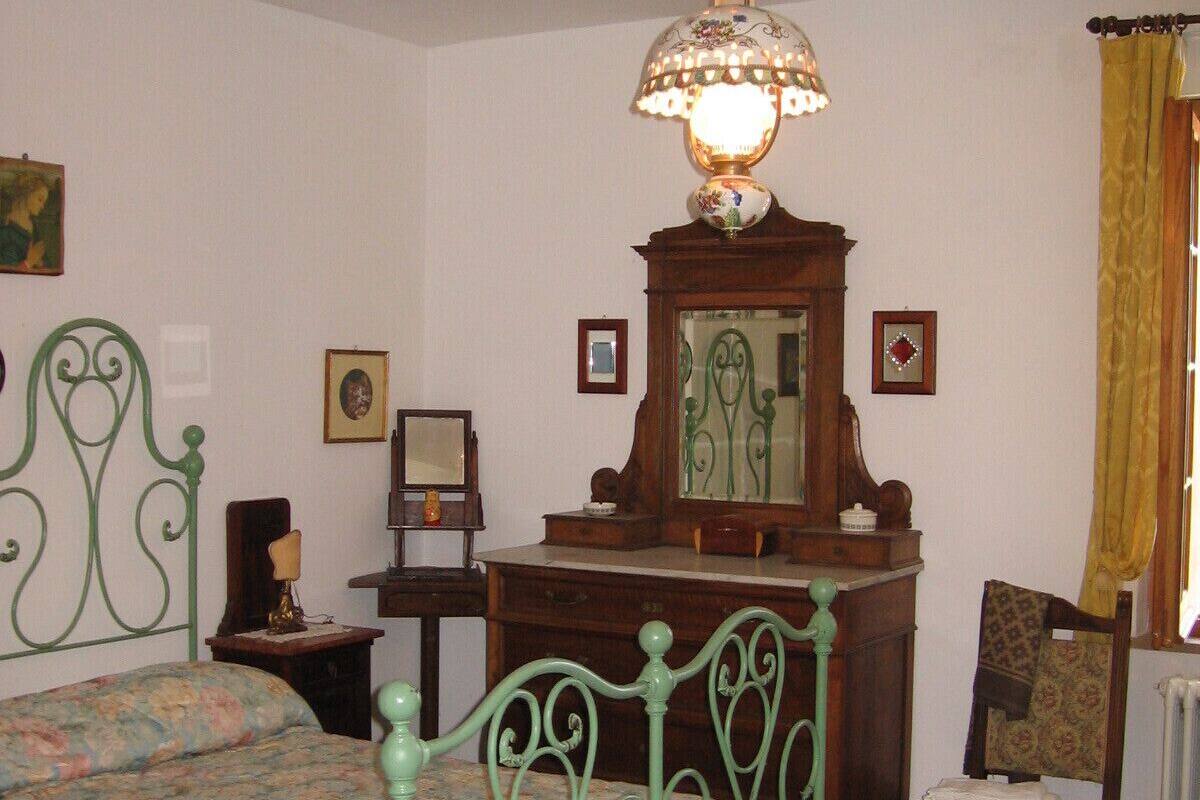 A bedroom with a green metal bed, a wooden dresser, a chair, a mirror, and a chandelier.