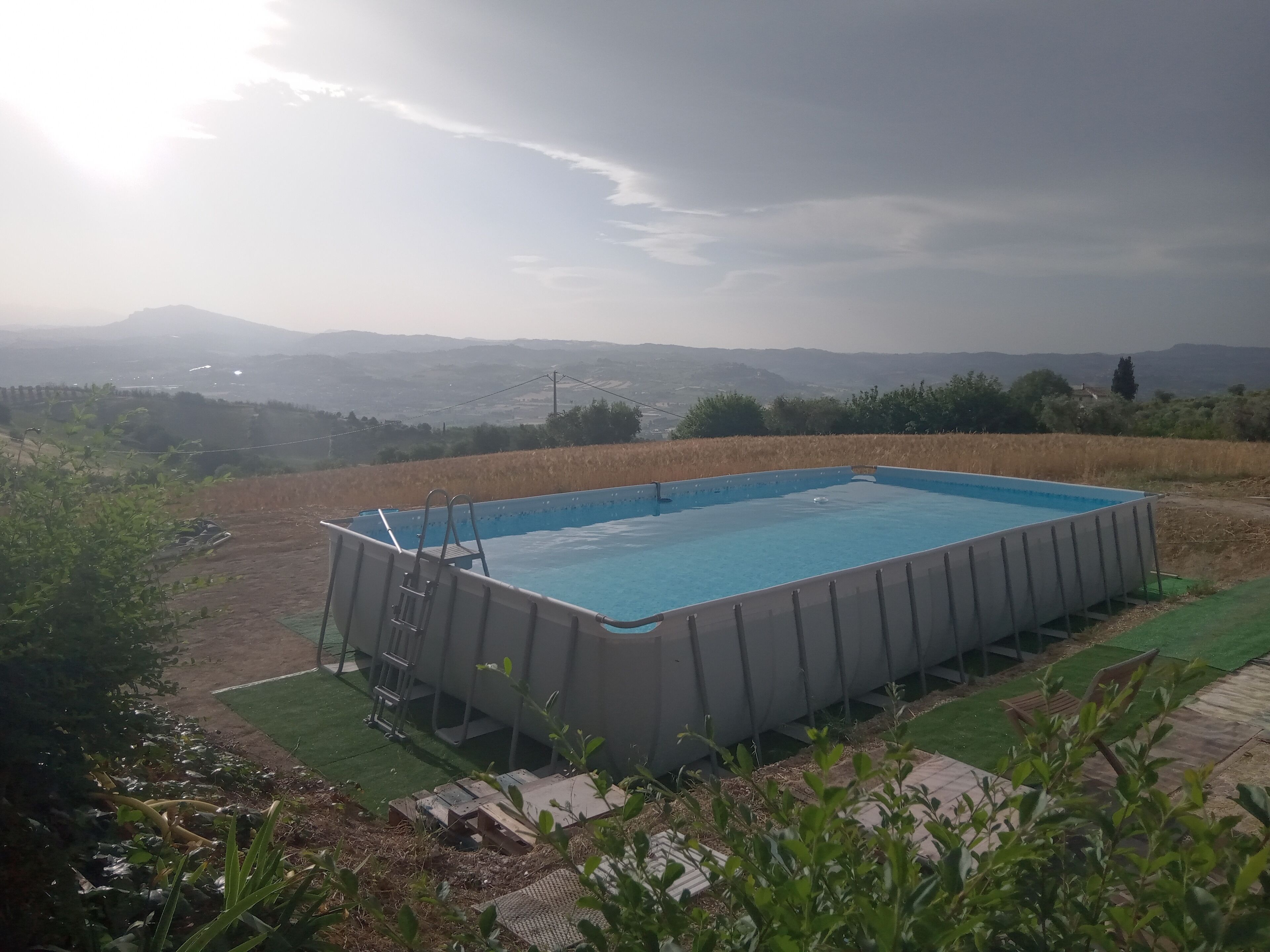 Piscina retangular com escada, cercada por um gramado e vista para colinas ao longe.