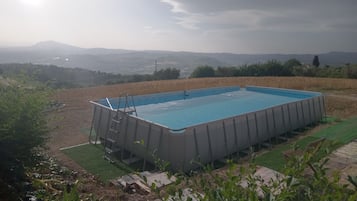 Piscina retangular com escada, cercada por um gramado e vista para colinas ao longe.