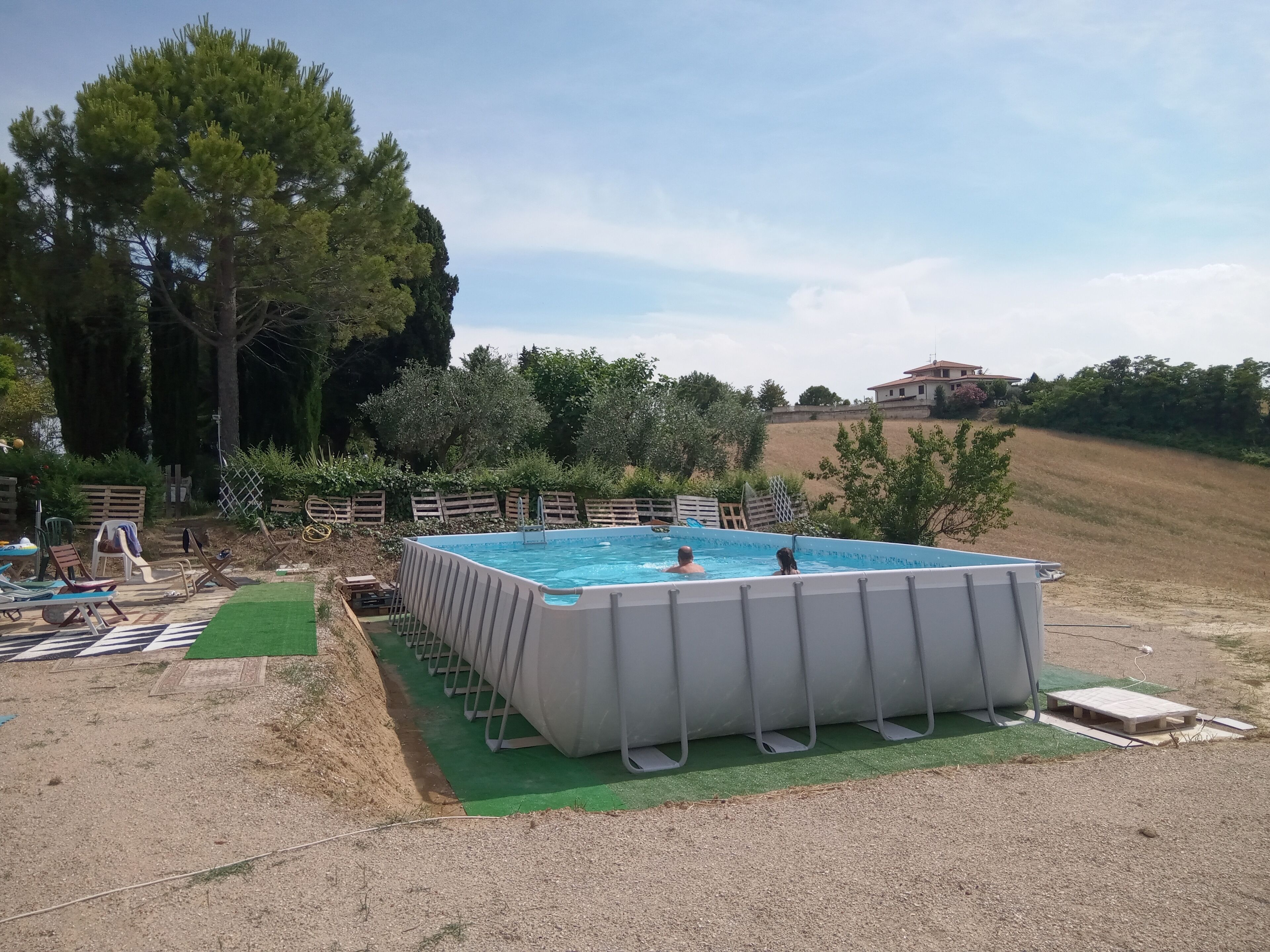 A rectangular swimming pool with a ladder, surrounded by a wooden fence and greenery.