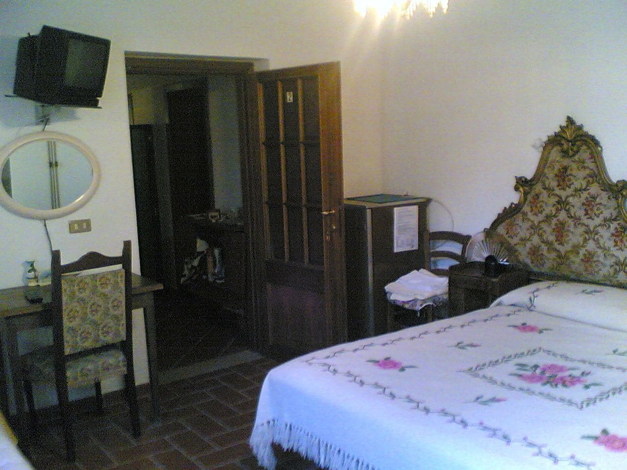 A bedroom with a bed, a chair, a desk, a mirror, and a television.