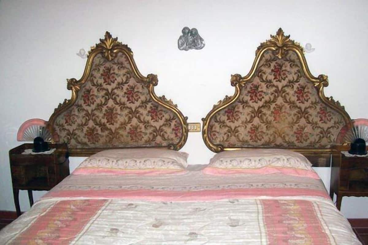 A double bed with ornate headboards, a bedside table with a lamp, and a decorative wall hanging.