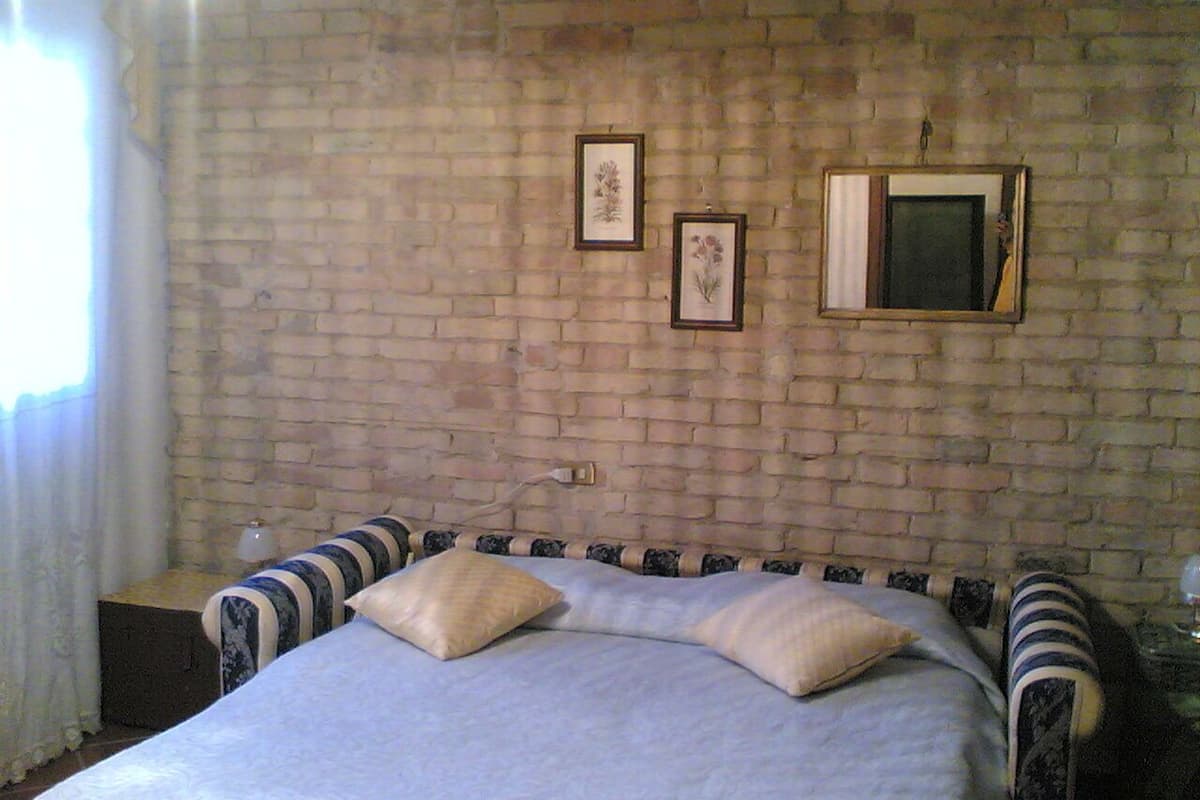 A bedroom with a brick wall, a bed with striped bedding, and two framed pictures.