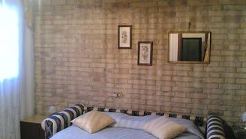 A bedroom with a brick wall, a bed with striped bedding, and two framed pictures.