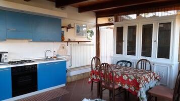 A kitchen with blue cabinets, a stove, and a sink. There is a dining table with chairs and a red tablecloth.