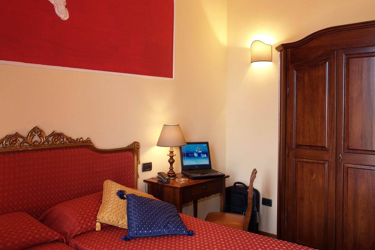 A hotel room with a bed, a desk with a laptop, a lamp, and a wardrobe.