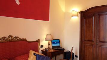 Ein Hotelzimmer mit Bett, Schreibtisch, Laptop, Lampe und Kleiderschrank.