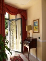 Una habitación con un piano, un cuadro en la pared y un ventanal con cortinas.