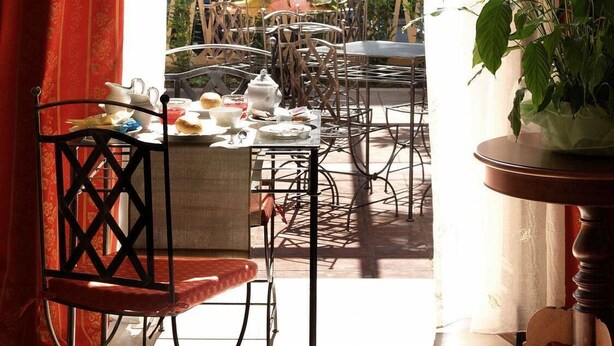 An outdoor dining area with metal chairs and tables, a wooden pergola, and a view of a building with a green door. - Petit Château (Montecatini Terme)