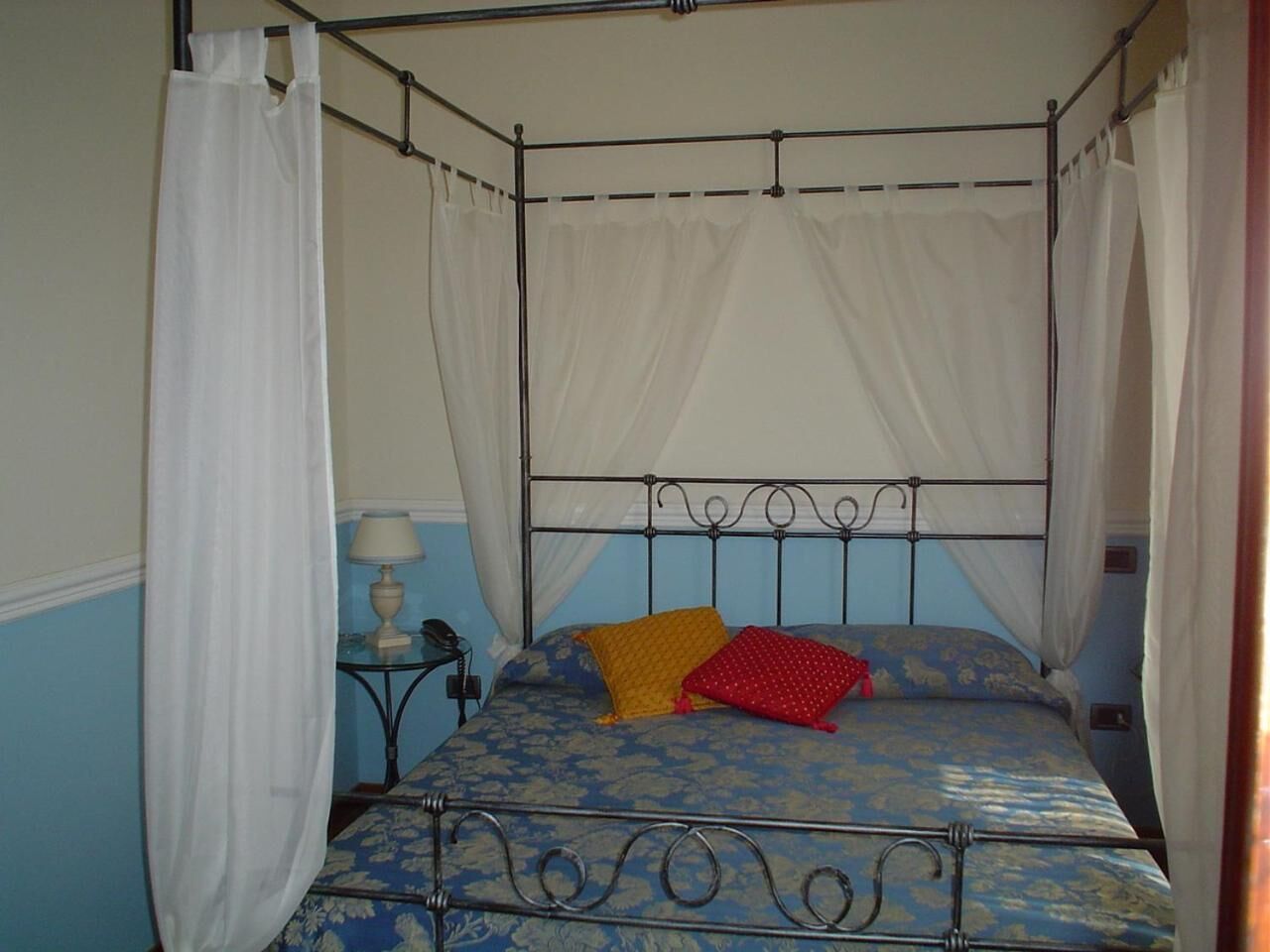 Ein Bett mit Baldachin, ein kleiner Nachttisch mit Lampe und zwei Kissen.