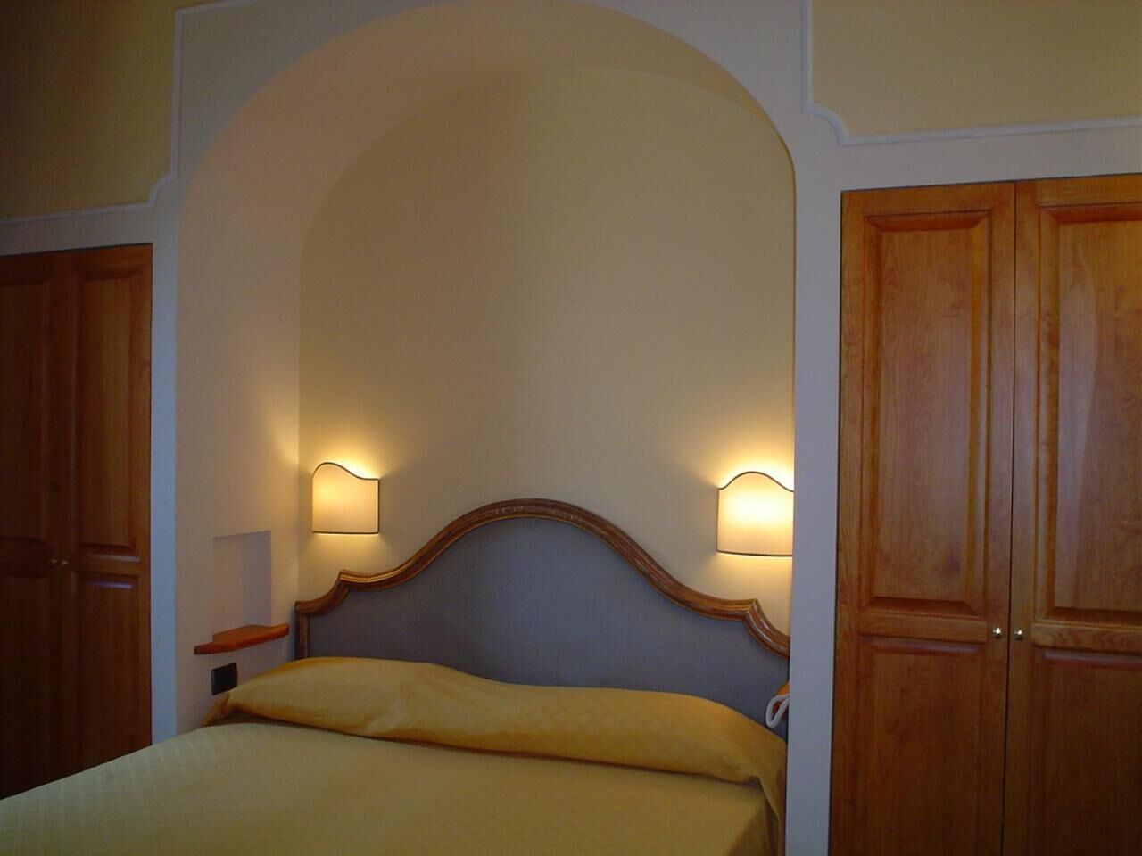 A bedroom with a bed, wooden wardrobe, and two wall-mounted lamps.