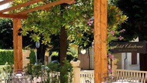 An outdoor patio with metal tables and chairs, surrounded by greenery and a wooden pergola. - Petit Château (Montecatini Terme)