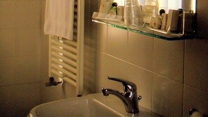 Un baño con lavamanos blanco, un espejo, toallero y repisa de vidrio con artículos de aseo.
