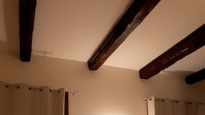 Un baño con dos cortinas atadas en la parte inferior, una lámpara de pared y vigas de madera en el techo.