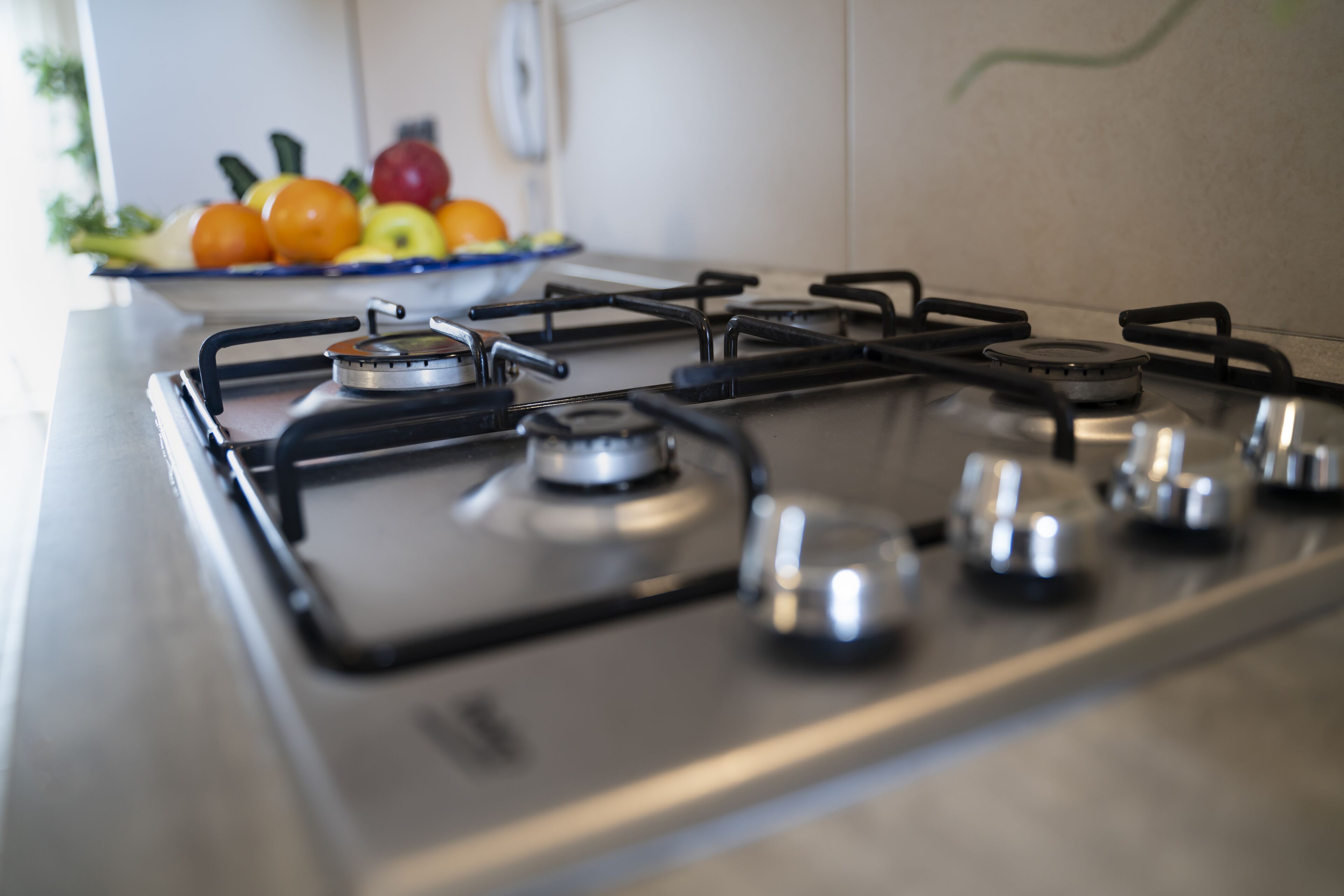 Una cocina con estufa a gas y un plato de fruta al fondo.