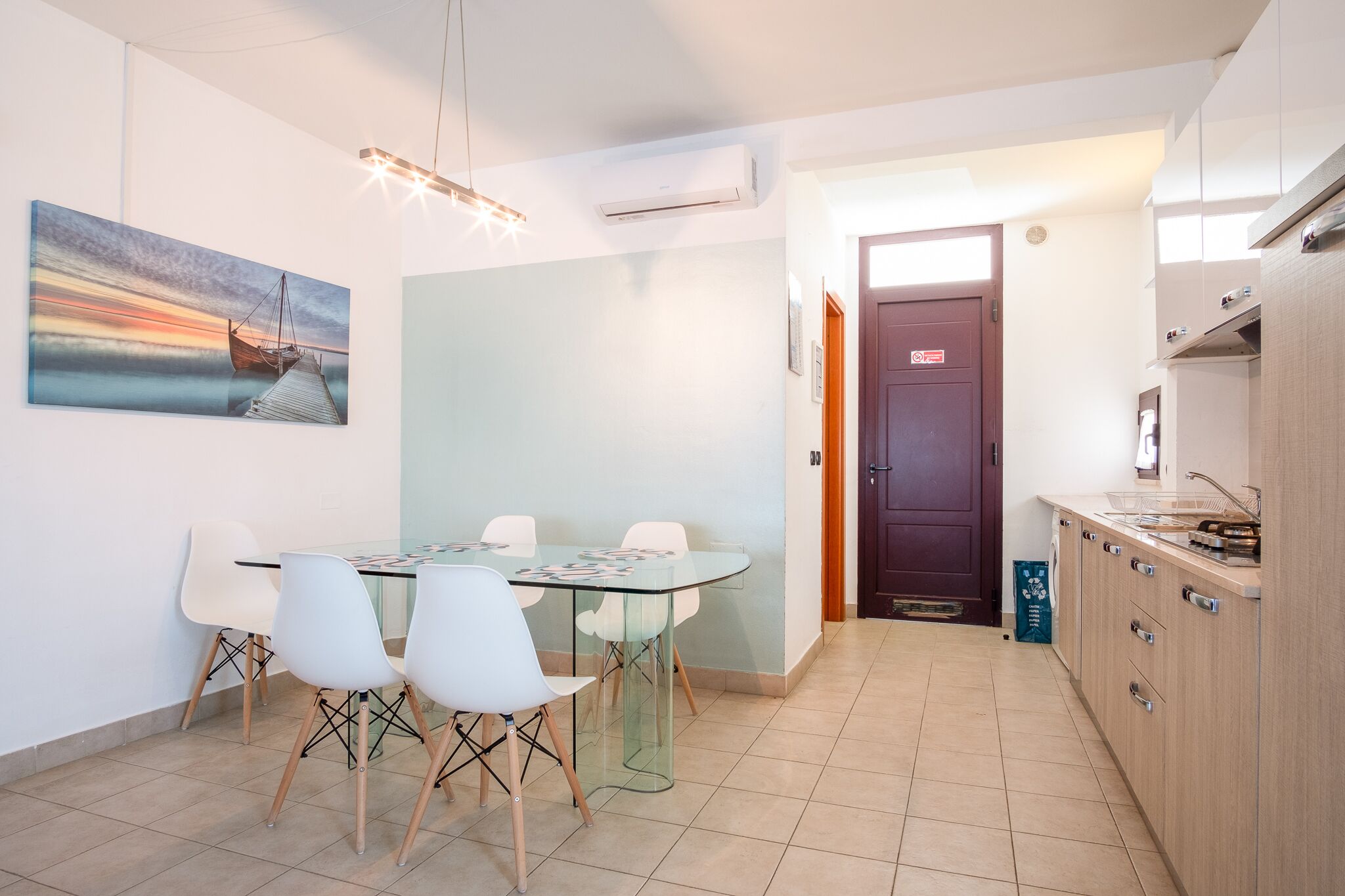 Una cocina moderna con un armario de madera, una mesa de vidrio y sillas blancas.