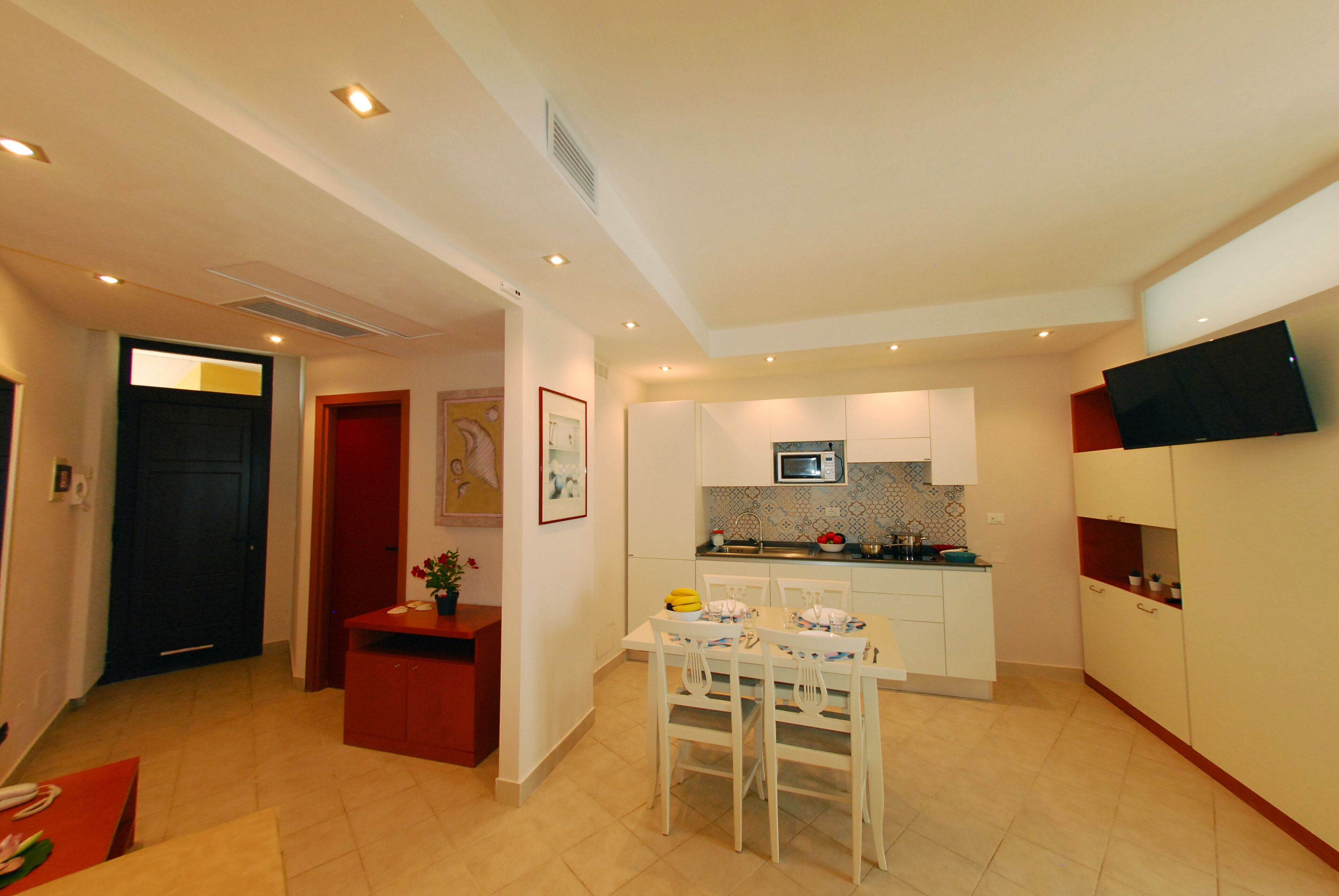 A compact living space with a dining area, kitchenette, and a TV mounted on the wall.