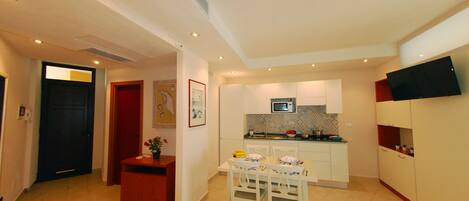 A compact living space with a dining area, kitchenette, and a TV mounted on the wall.