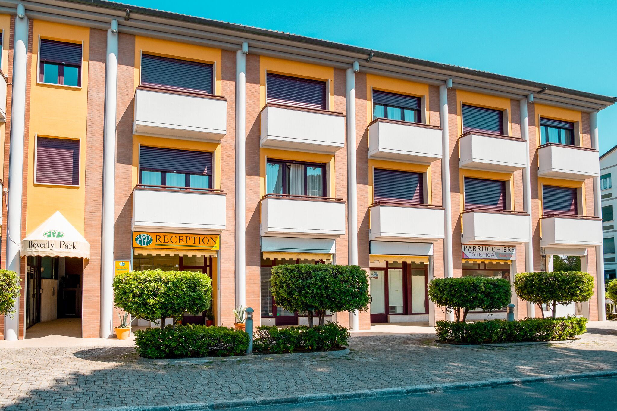 Un hotel de varios pisos con fachada amarilla, múltiples balcones y una recepción.