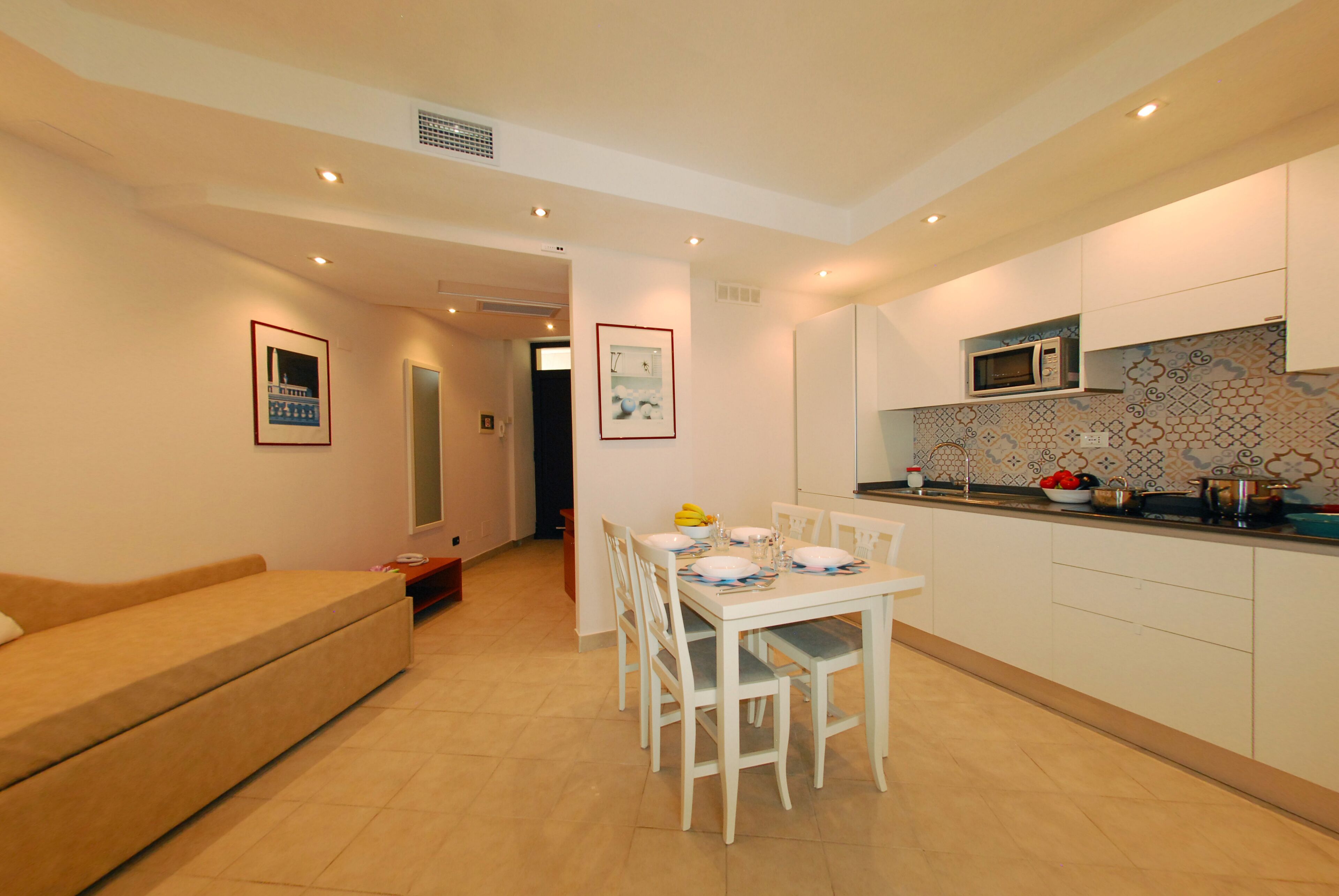 A modern kitchen with white cabinets, a dining table set for four, and a microwave above it.