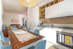 A modern kitchen with white cabinets, a built-in oven, and a dining area with a wooden table and blue chairs.