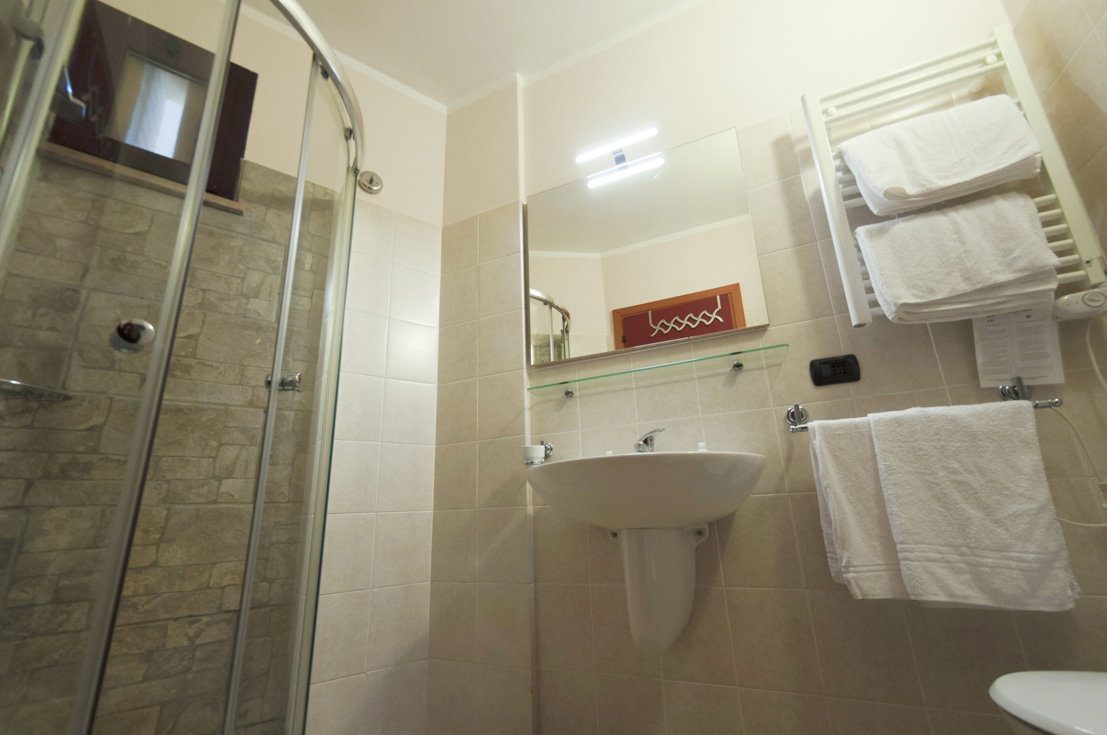 Un baño con cabina de ducha de vidrio, un lavabo y un perchero con toallas.