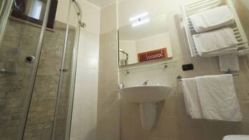 Un baño con cabina de ducha de vidrio, un lavabo y un perchero con toallas.