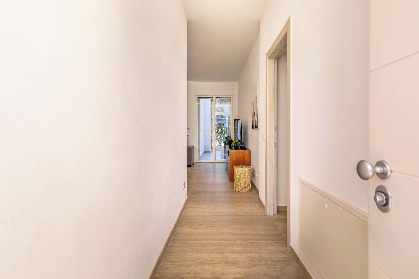 Un couloir avec un plancher en bois, des murs blancs et une porte sur le côté droit.