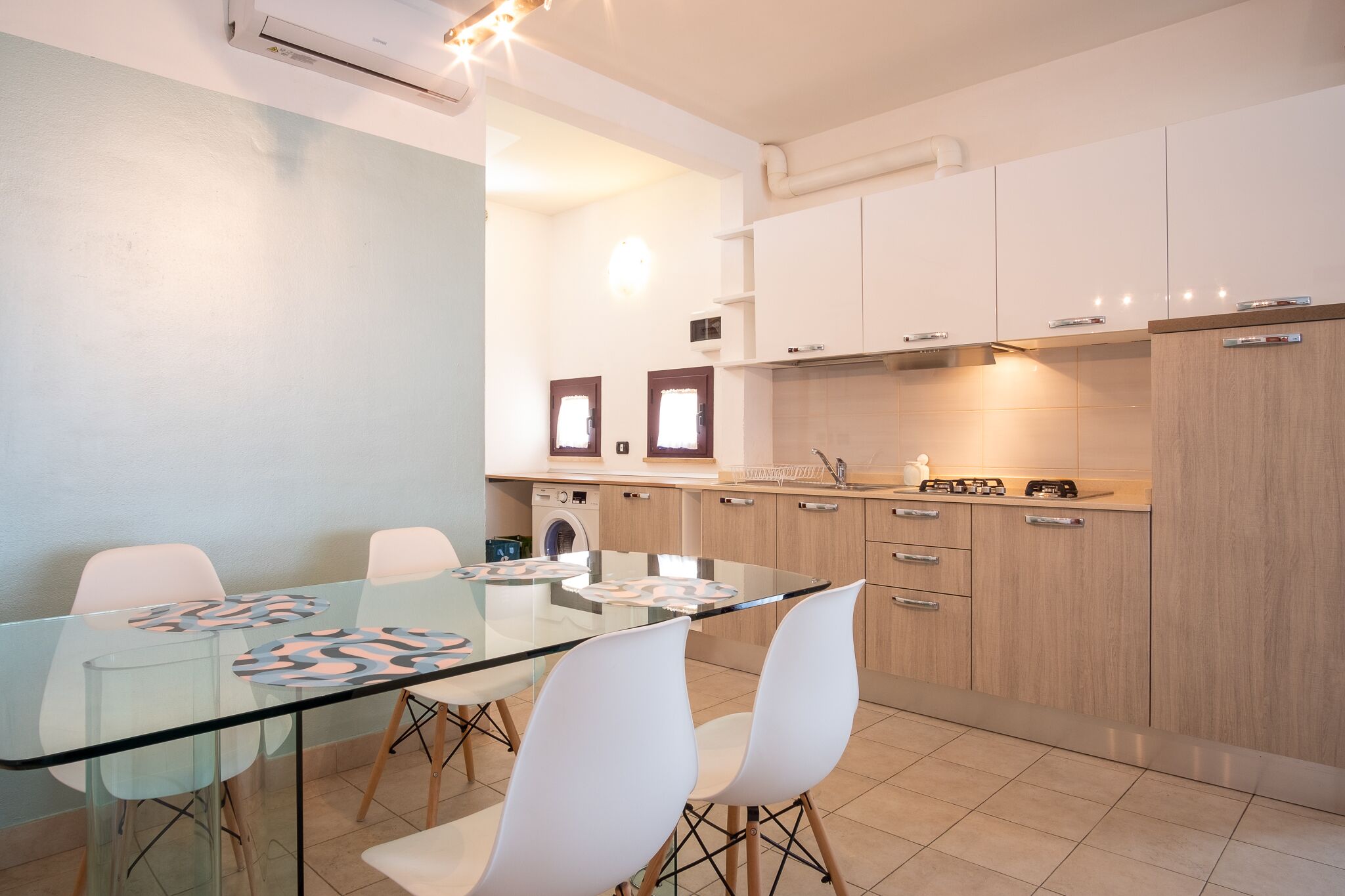 Une cuisine moderne avec des meubles blancs, une table à manger en verre et un lave-linge encastré.