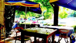 An outdoor dining area with tables and chairs under umbrellas, surrounded by greenery. - Shine (Acqualagna)