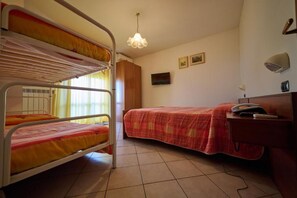 A room with bunk beds, a single bed, a desk with a telephone, and a wall-mounted lamp.
