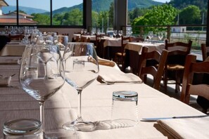 A restaurant with tables set for dining, clear glassware, and a view of greenery and mountains.