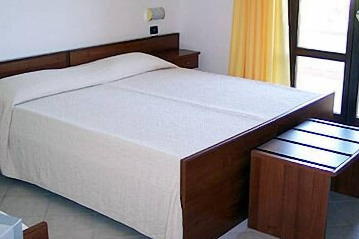 A bedroom with a wooden bed, a bedside table, and a window with curtains.