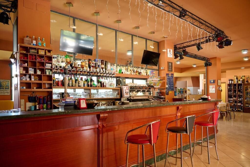A bar with a wooden counter, red bar stools, and shelves stocked with bottles.