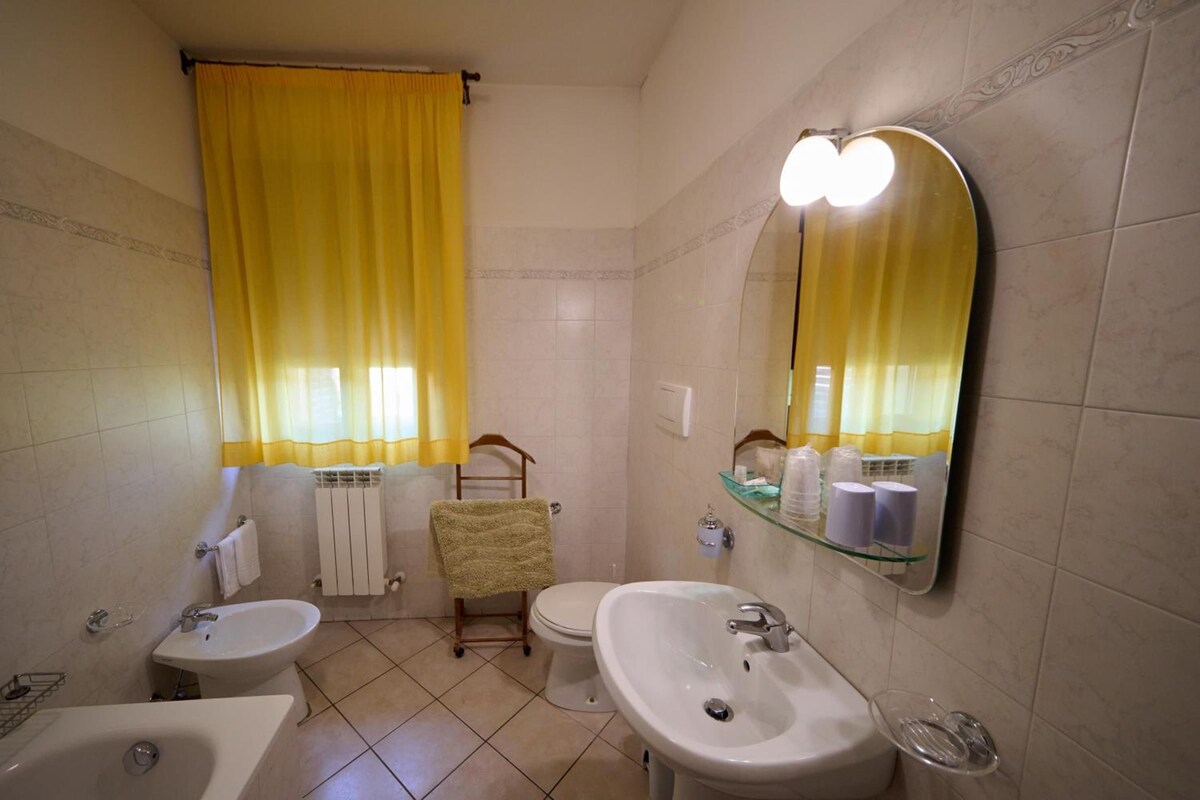 A bathroom with a bathtub, two sinks, a toilet, a towel rack, and a mirror with lights.