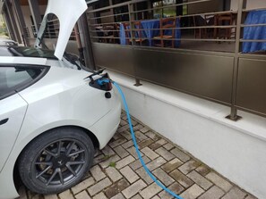 A white car parked next to a building with a blue hose connected to it. - Shine (Acqualagna)