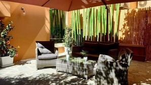 Une terrasse ensoleillée, meublée de meubles en osier, avec un canapé confortable et un paravent en bambou.