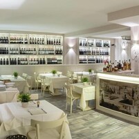 Interno di un ristorante con diversi tavoli, sedie e una parete dedicata all'esposizione di vini.