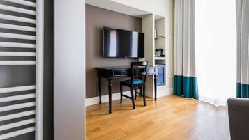 Habitación de hotel con una televisión de pantalla plana montada en la pared, un escritorio de madera con una silla y un ventanal con cortinas.