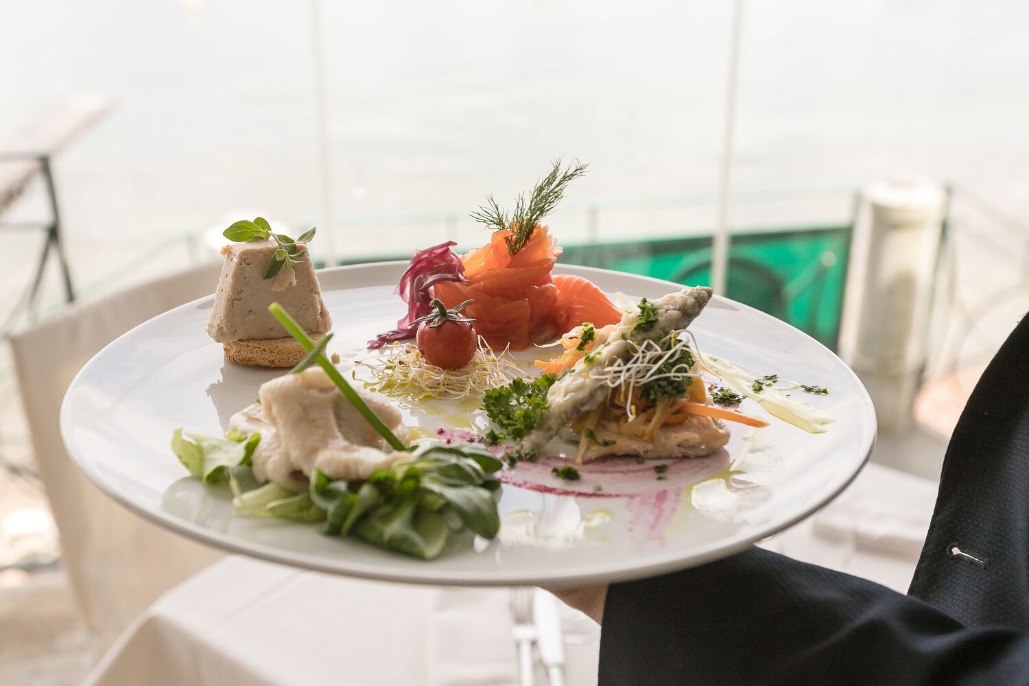 Een bord eten met verschillende gerechten, waaronder zalm, een kleine paté en groenten, geserveerd op een wit bord.