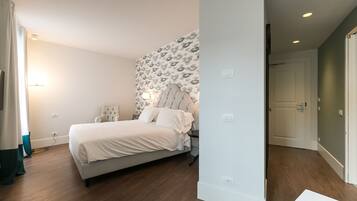 Un dormitorio con cama, una silla, una mesita de noche, una pared con papel tapiz estampado y una puerta.