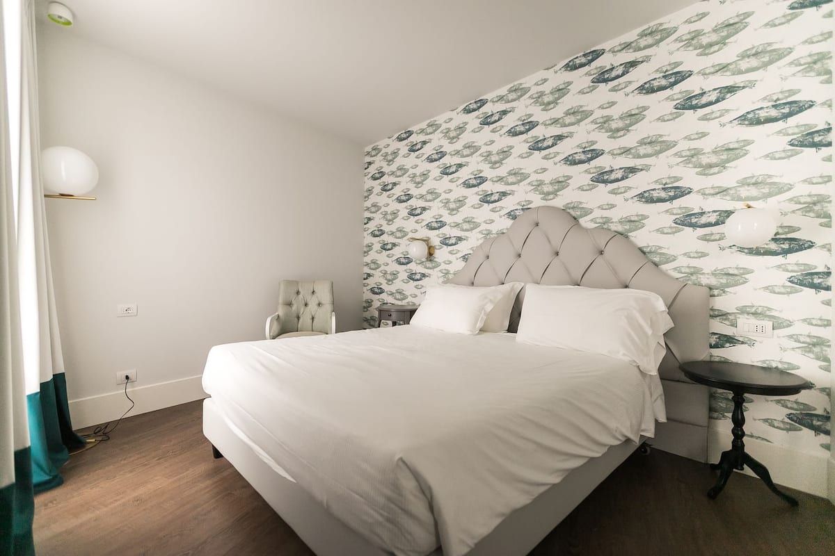 A bedroom with a bed, a chair, a bedside table, and a wall with a fish pattern.