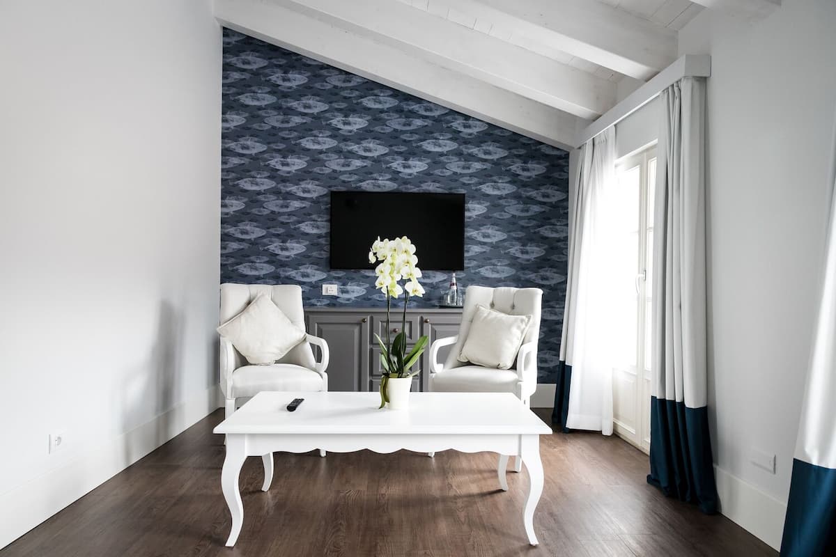 A modern living room with two white armchairs, a white coffee table, and a large TV mounted on a patterned wall.