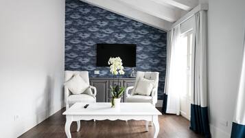 Un salon moderne avec deux fauteuils blancs, une table basse blanche et un grand téléviseur fixé au mur, qui est décoré d’un motif.